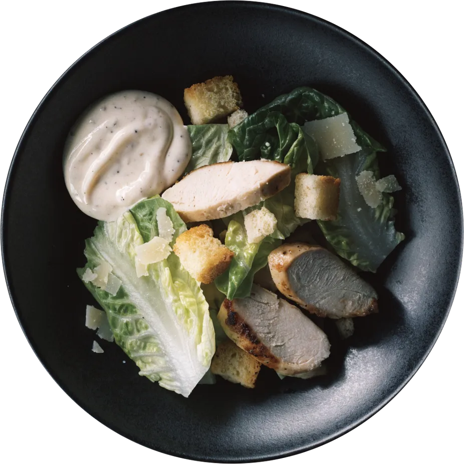 A chicken Caesar salad on a dark plate, from above
